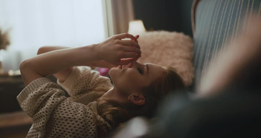A woman is sitting on the floor leaning against a couch and doing dance moves with her hands and arms