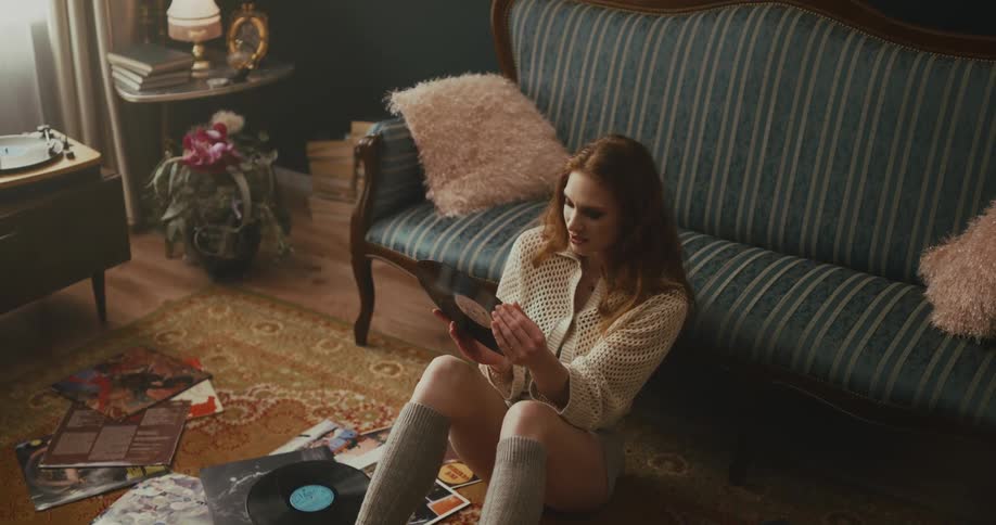 A woman sitting on the floor in the living room listening to record albums