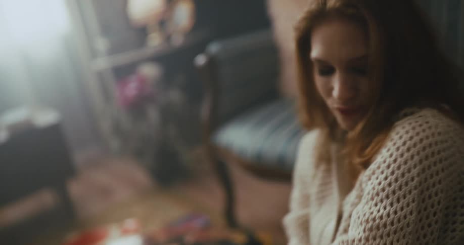 A teenage girl leans against a couch at home and dances to a record playing on a vintage record player