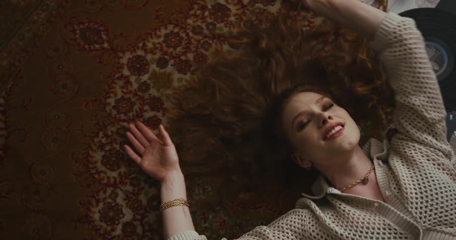 A woman listens to a vinyl album and dances while lying on the floor