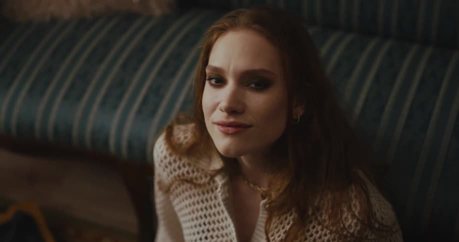 A teenage girls leans against a couch at home and moves to music playing on a vintage record player