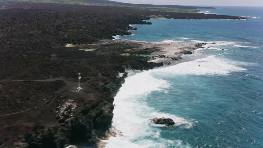 Water sparkles as the waves roll into shore and crash against the rocks along the coast and there are mountains on the horizon