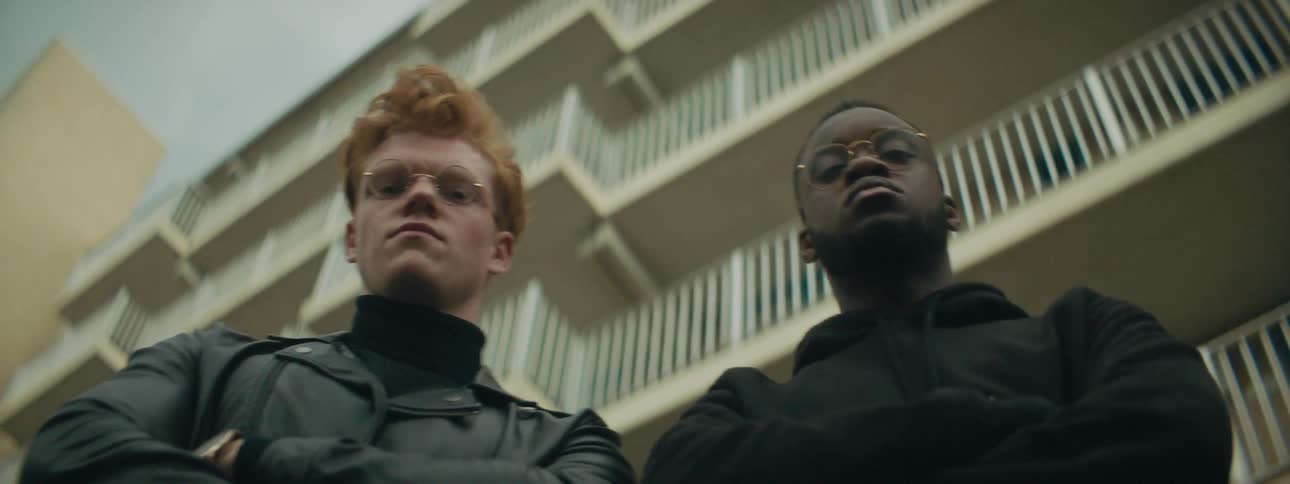 Two scowling men standing next to a building in the daytime