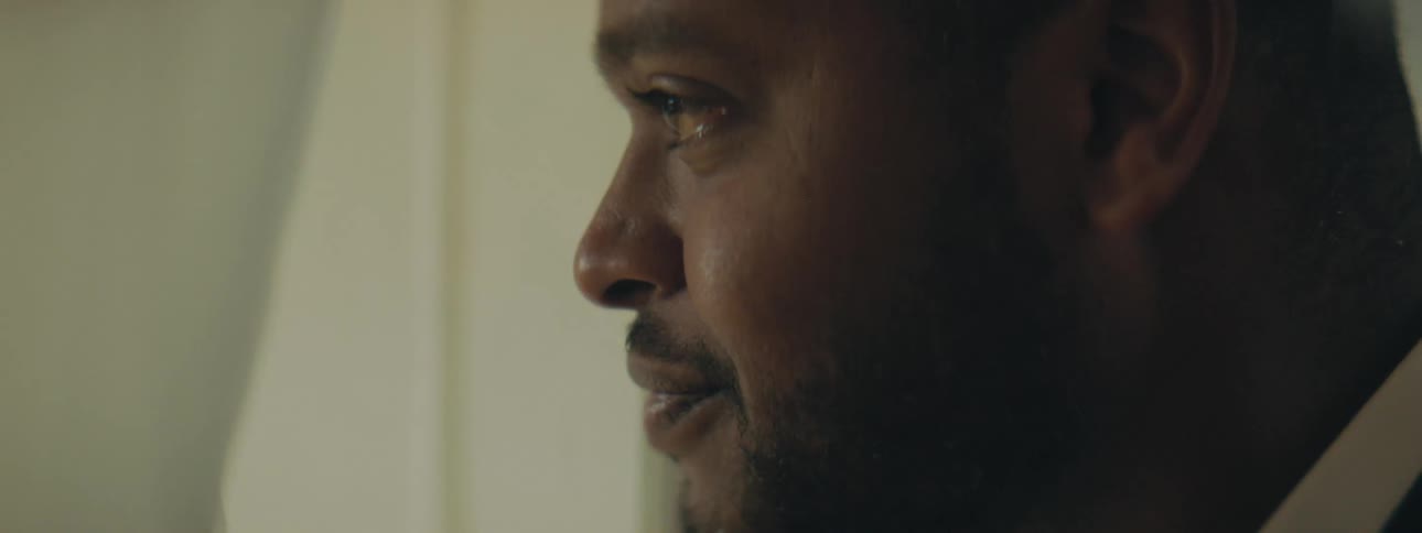 A man parts a curtain to gaze out through the window