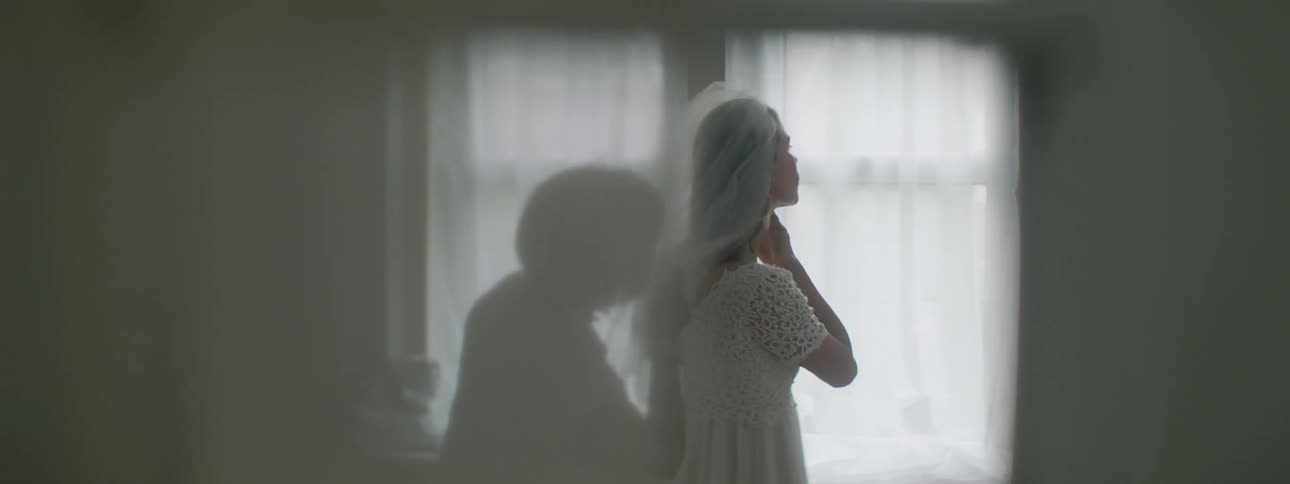 A woman helps a bride with her bridal veil then blocks a doorway quickly from being seen