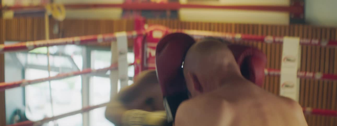 A pair of men box in the boxing ring of a gym during the day
