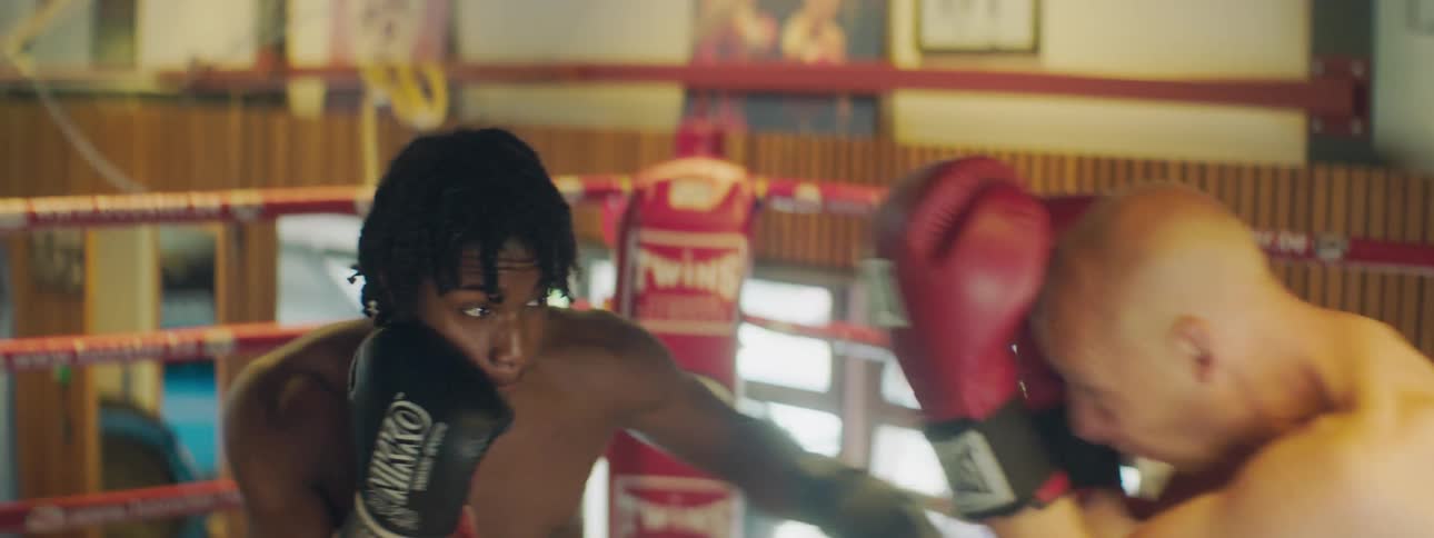Two men spar in a boxing ring in a gym