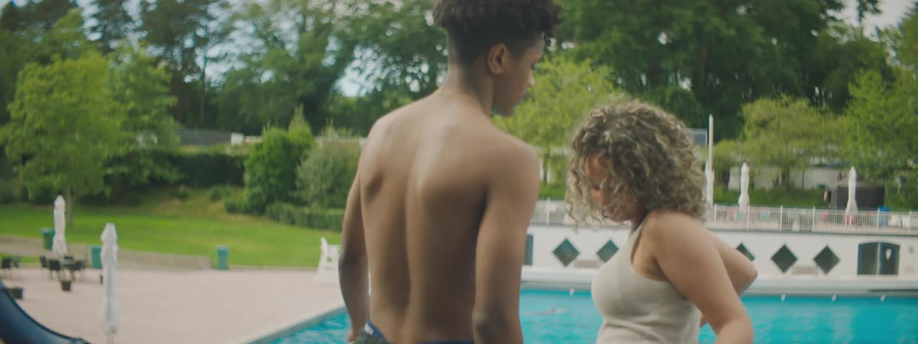 A male and female stand beside the pool with flirtatious movements