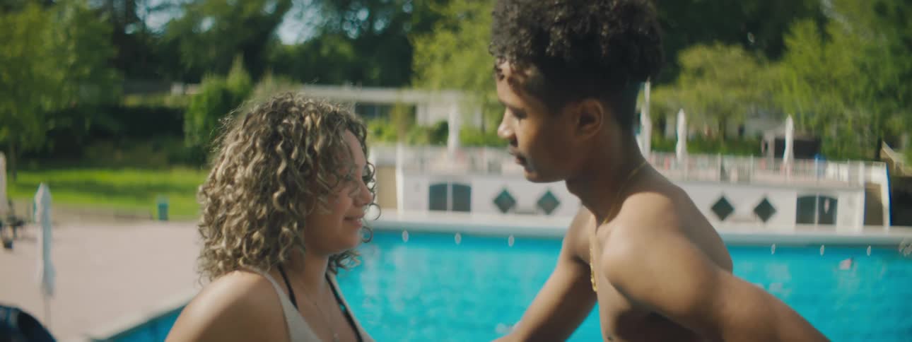 A man leans into and kisses a woman as they stand by an outdoor pool