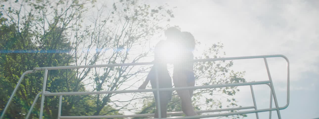 Black male walks across a platform and kisses a caucasian woman on a sunny day
