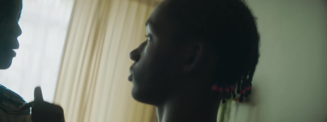 A woman and a boy standing in a room talking with a window and curtains in the background