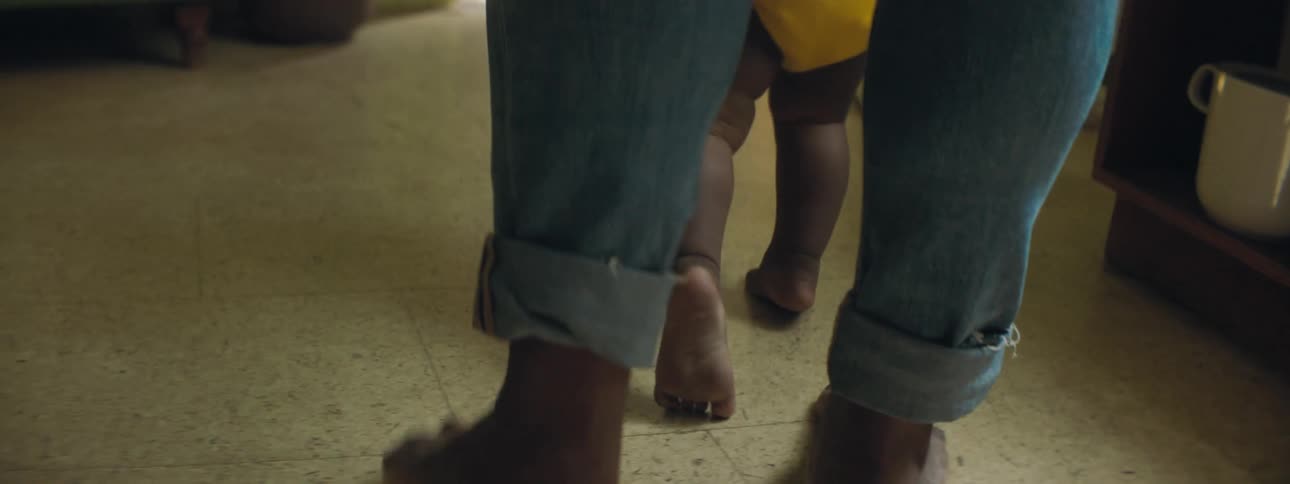 Mother with ripped jeans walks toddler girl wearing yellow clothes in the living room