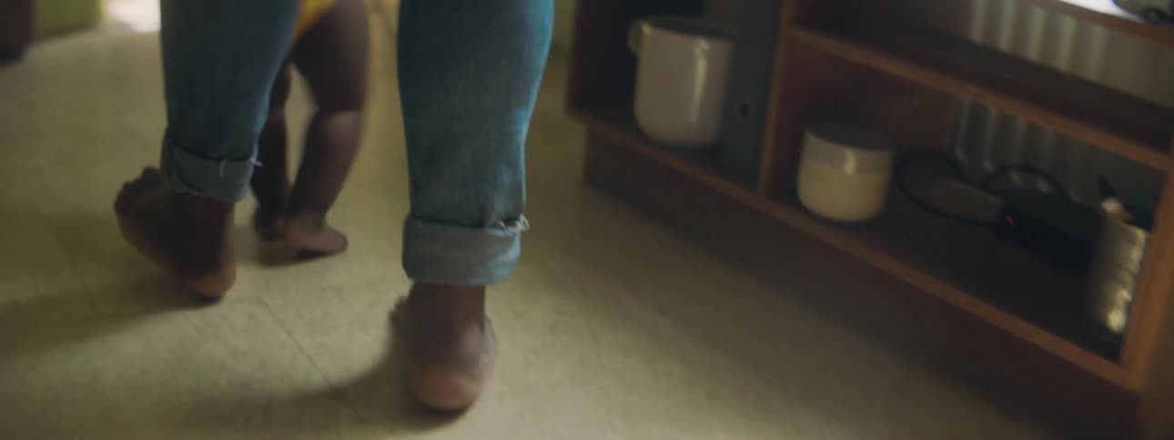 A parent holds the hands of their baby as they try walking across the living room