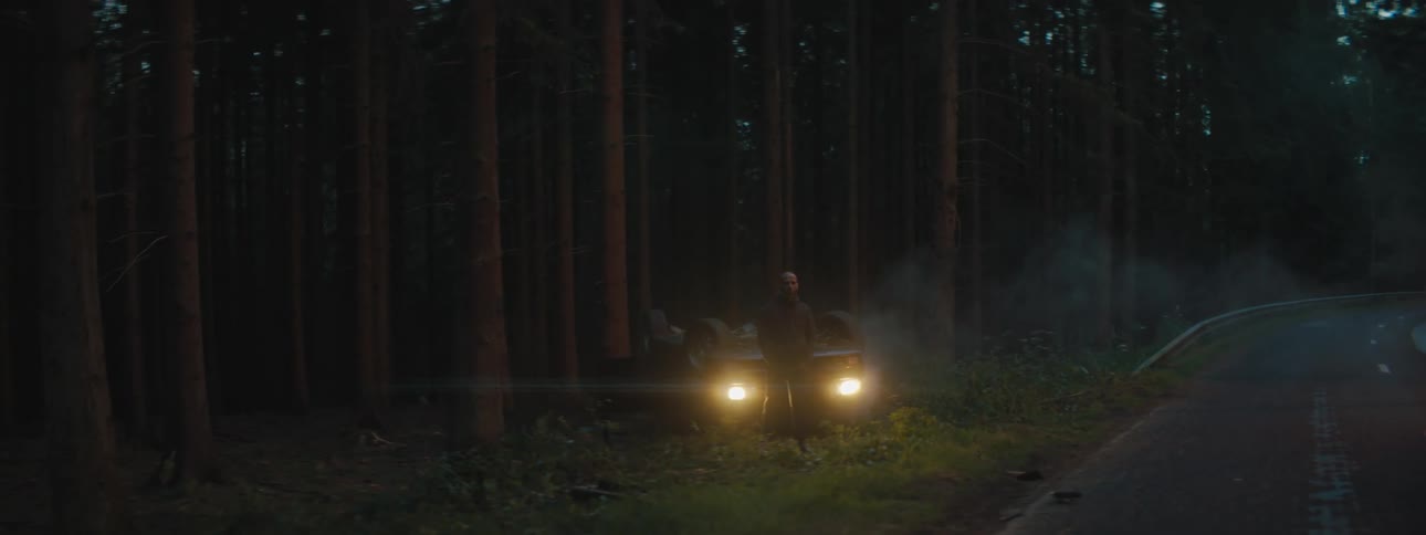 A man stands in front of his car in a forest