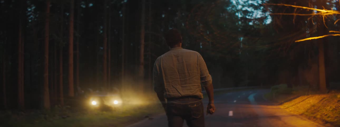 Sad and depressed man stands in the middle of a road looks at the car crash in the woods