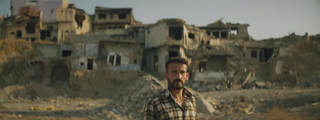 A man stands in front of ruins in a third world village