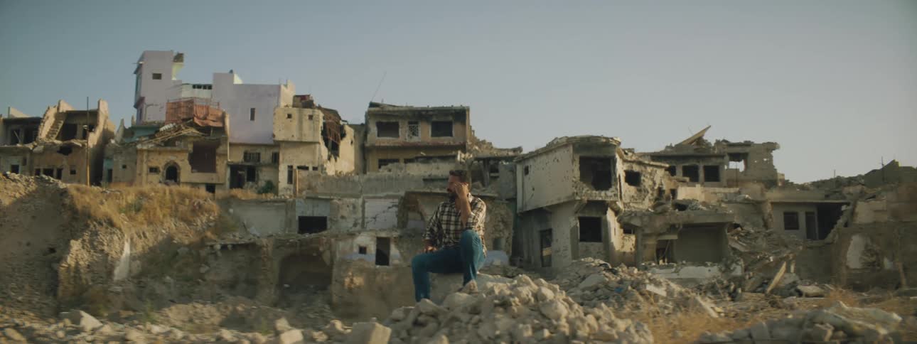 A man sits on a pile of debris and rubble in front of destroyed homes