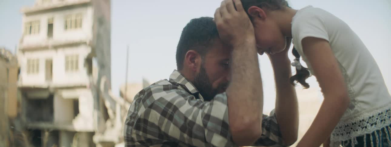 A man and a girl touching foreheads with buildings the sky and clouds in the background