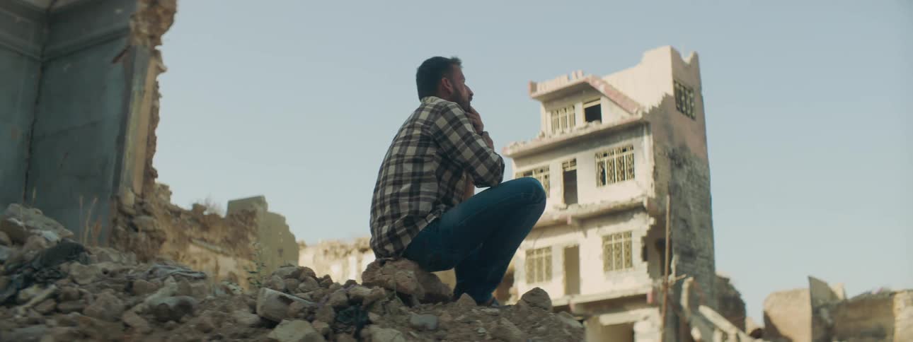 An upset man sits on rubble of a building in a town that has been destroyed