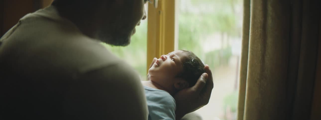 Father cradling and talking to newborn son near a window indoors