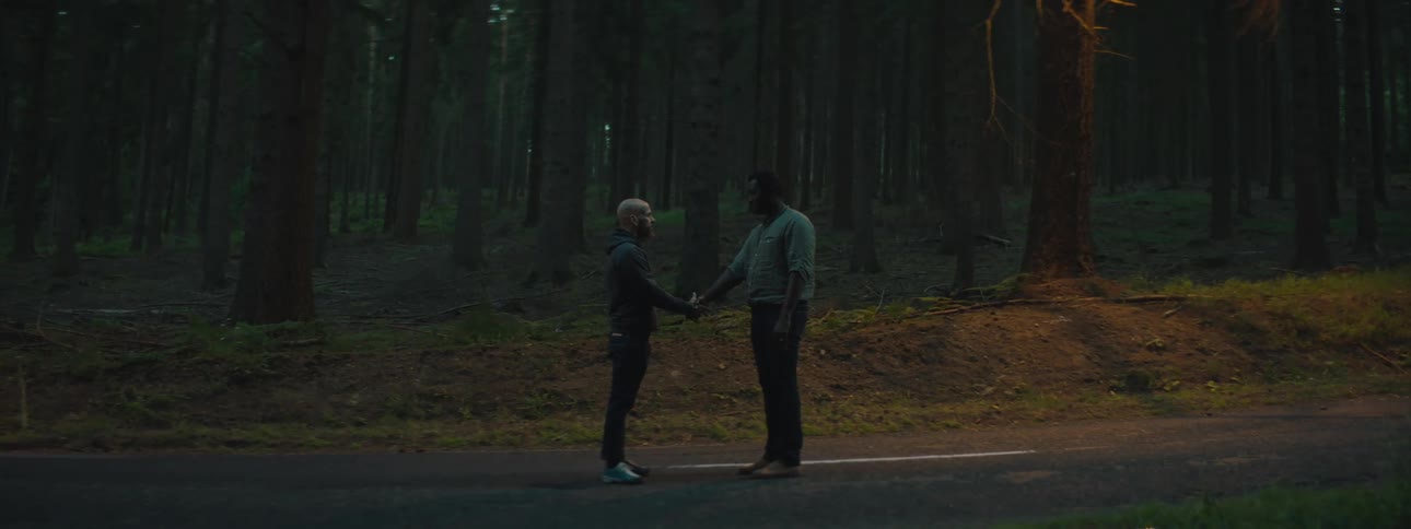 Two men are standing outdoors in a wooded area