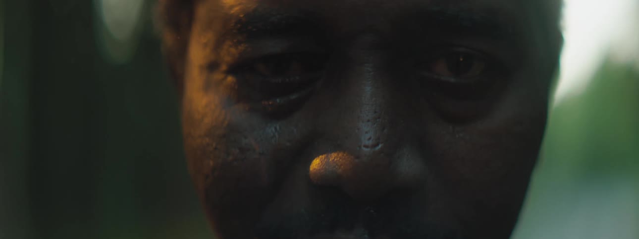 A middle aged black man stares into the camera while standing outdoors during the day