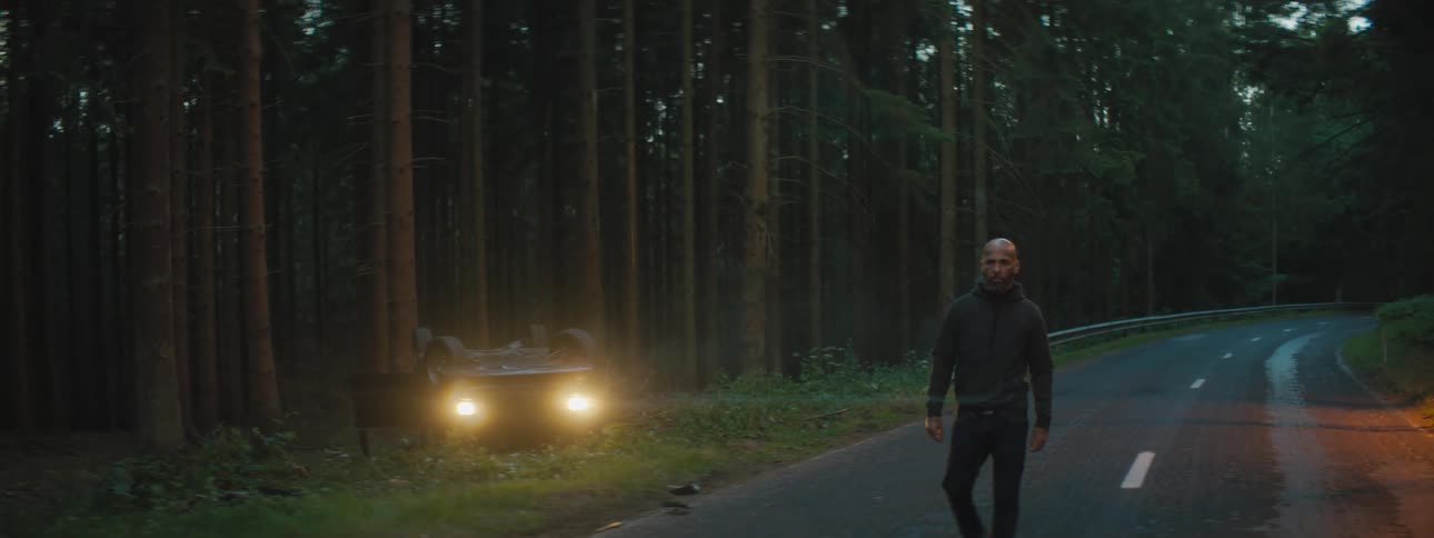 A man walking away from an upside car after a car accident in a forest