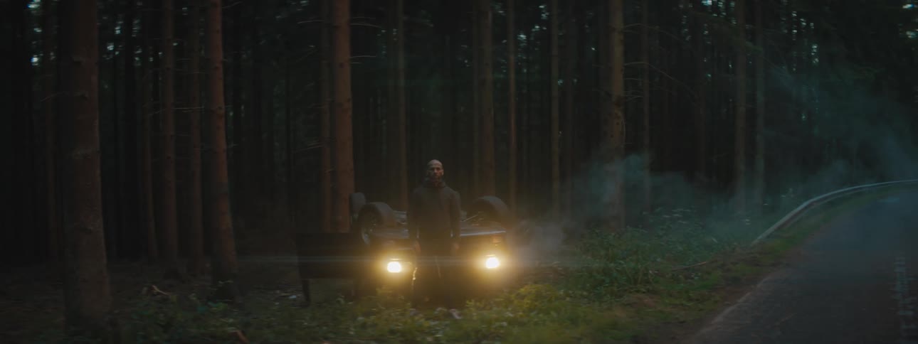 A man standing in front of an upside car after an accident in a forest