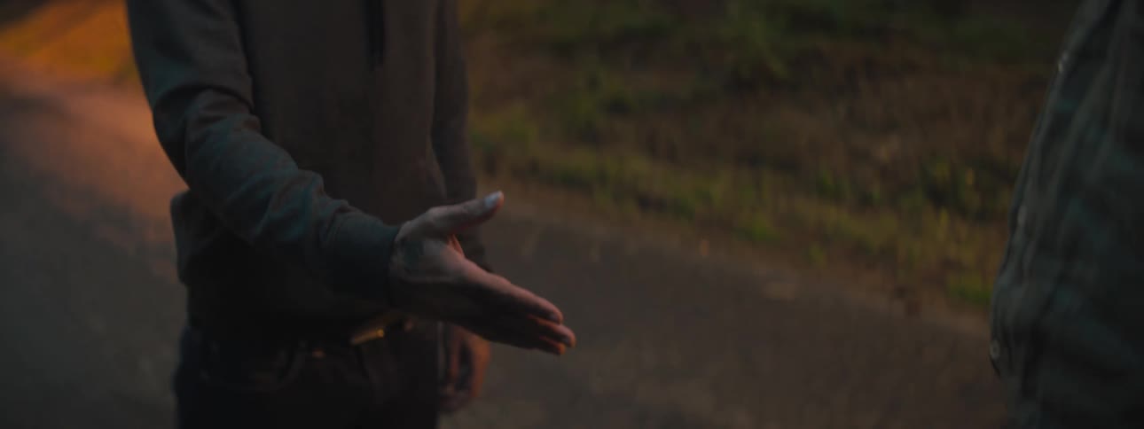 A man is shaking hands with a person outdoors at dusk
