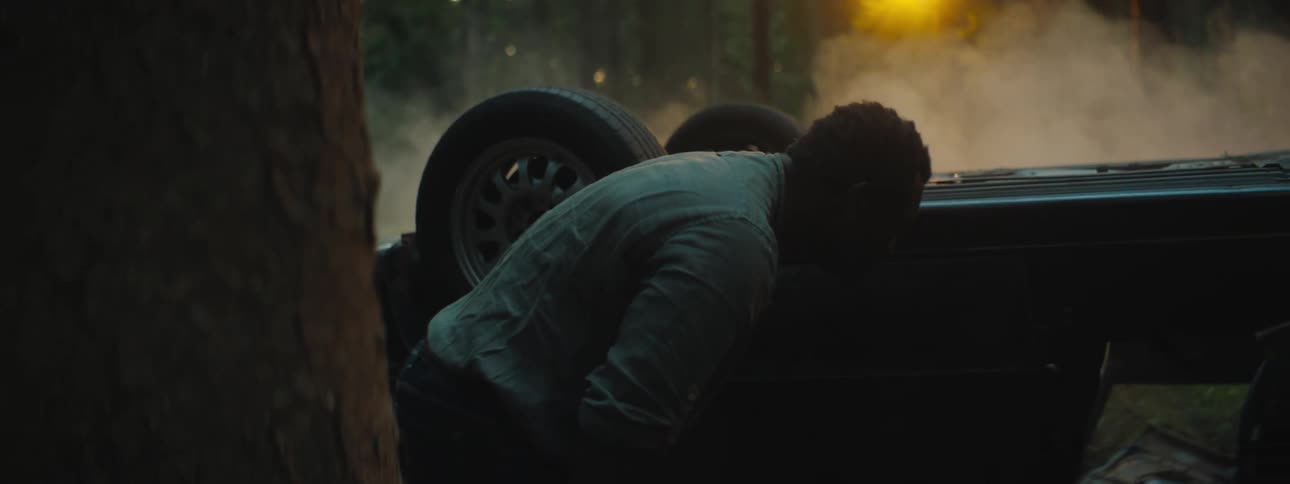 A man is checking on his flipped car in the forest