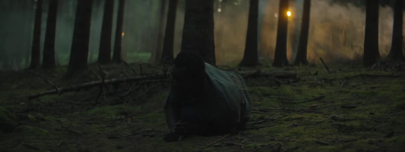 An injured man standing up in a dark forest at dusk