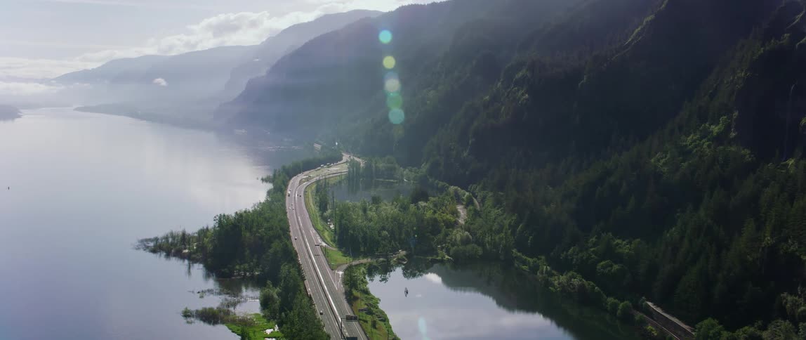 Aerial view of highway next to lake and high mountains on sunny day