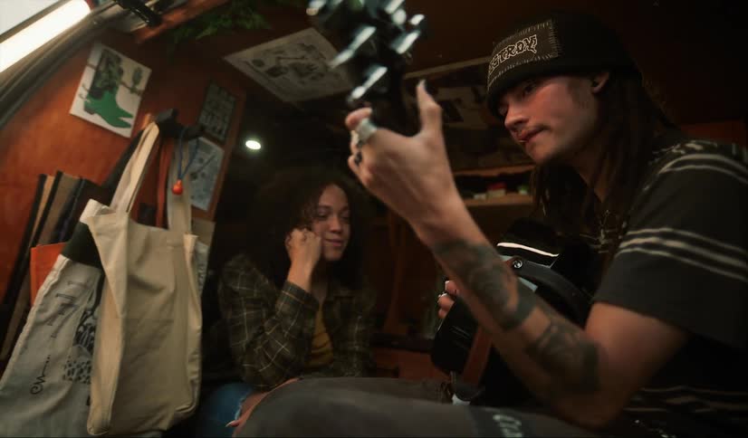 A woman sings along as her boyfriend plays guitar while they sit in their camper van