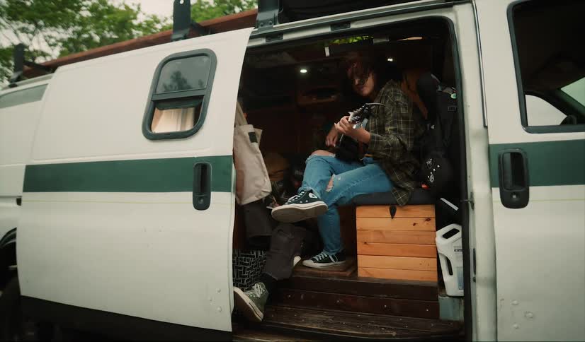 People are sitting in a campervan and one is playing guitar