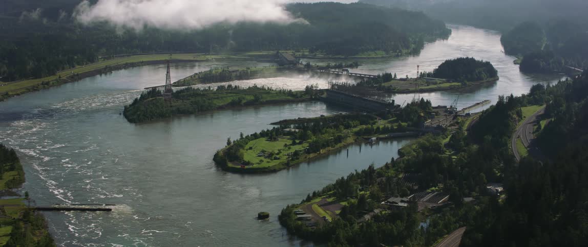 A road winds its way on the mountains next to a river with islands and buildings