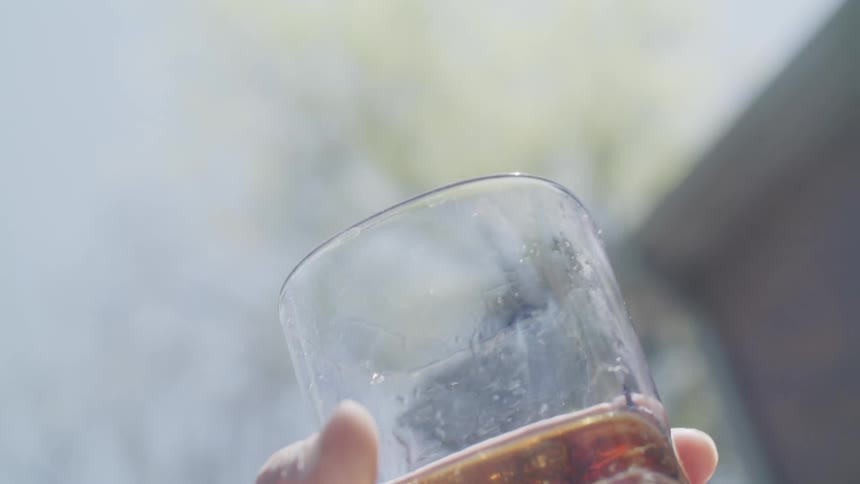 A hand holding a drinking glass with a flaming lit sprig inside with amber liquid