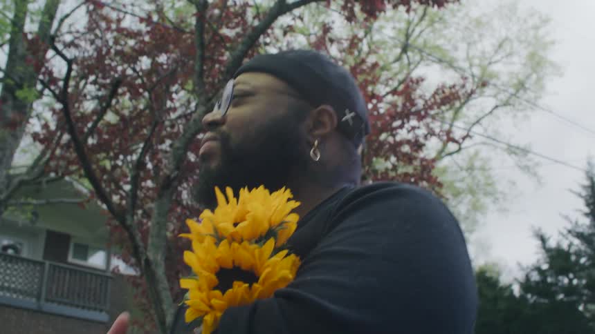 A man cradles a bouquet of yellow flowers while walking through a neighborhood during the day