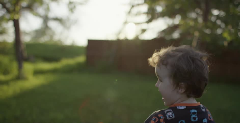Young boy runs across lawn in field near fenced yard