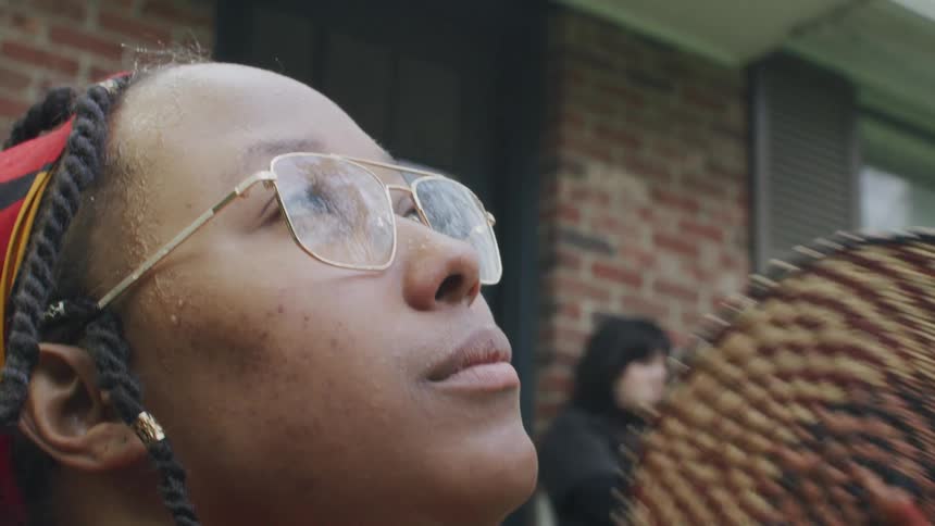 Woman with dreadlocks and glasses uses brown folding fan looking up in the sky