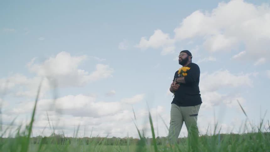 A man is walking through a field carrying yellow flowers
