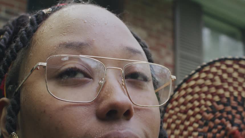 Girl with dreadlocks and glasses uses folding fan looking down at camera