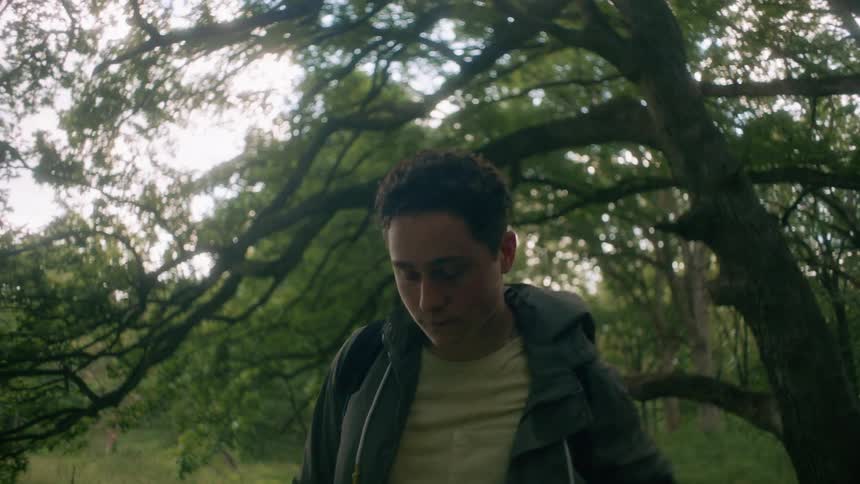 A teenage boy in a forest takes a deep breath and takes off his back pack