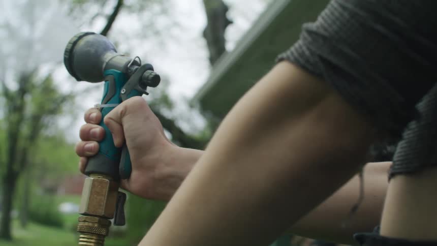 A woman is spraying with a hose near a house