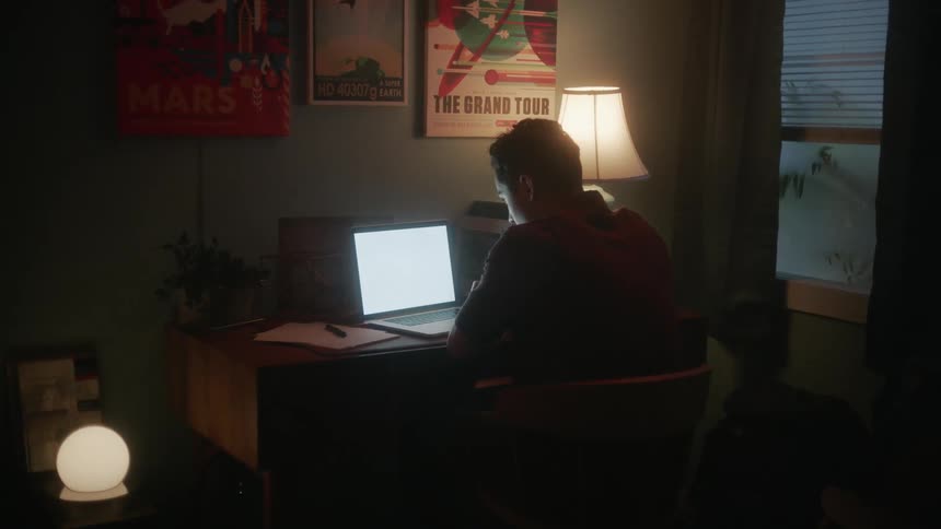 Man sits at desk viewing laptop screen at night