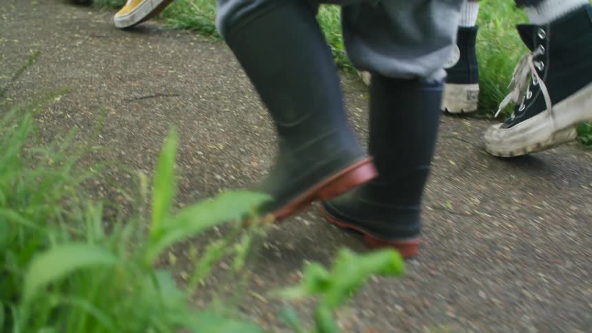 Close up of the rubber boots of a boy walking on a path in the backyard