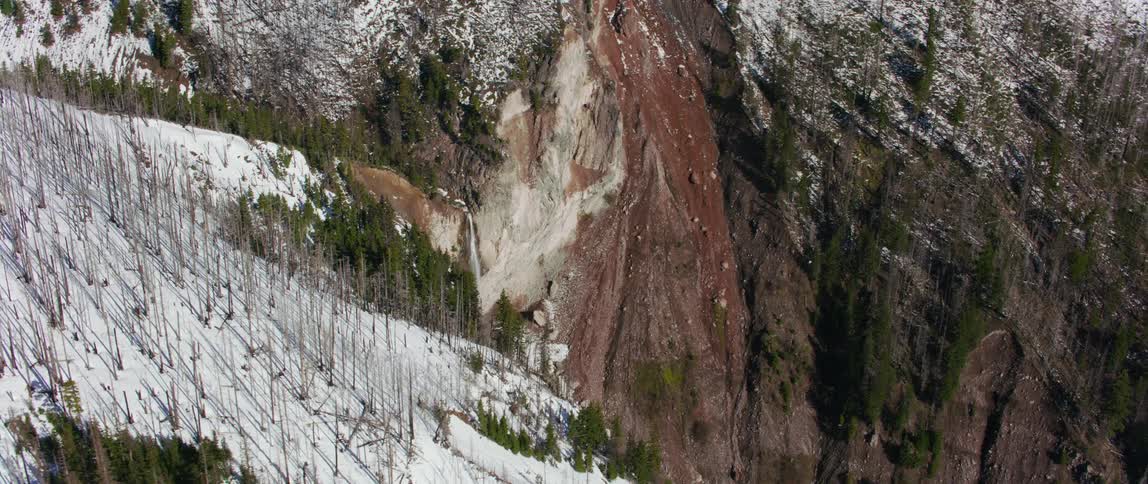 A mountain slope leads to a sheer cliff and flowing waterfall