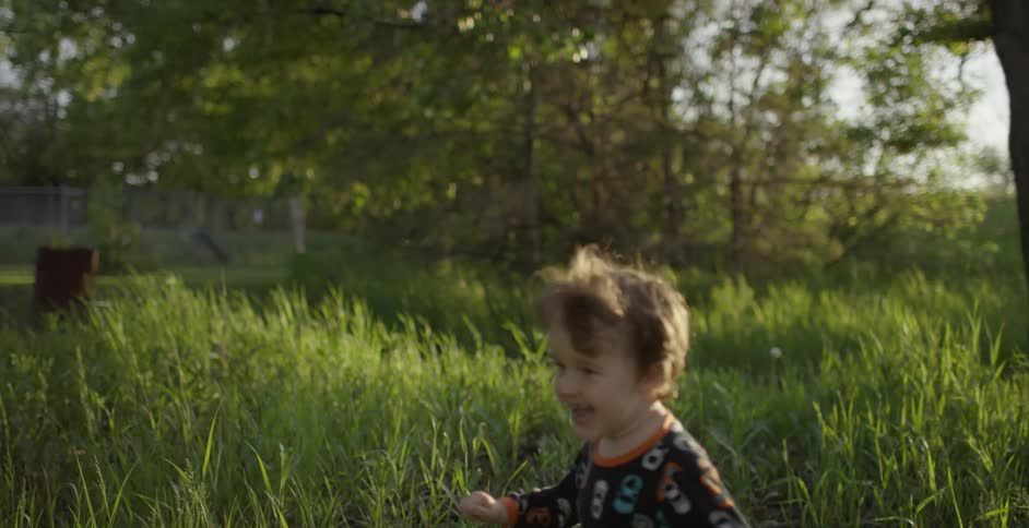 A young boy laughs as he runs around a tree in his backyard