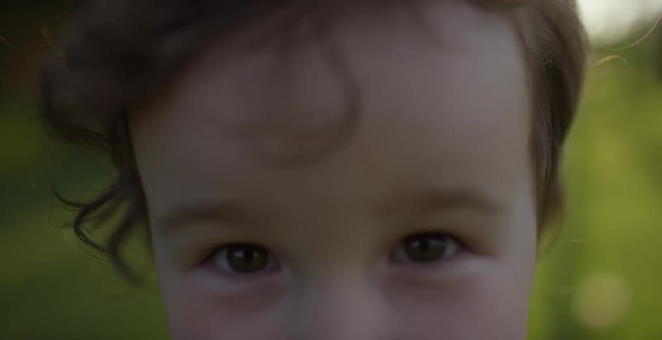 A child standing outdoors looks into the camera for a moment before looking away