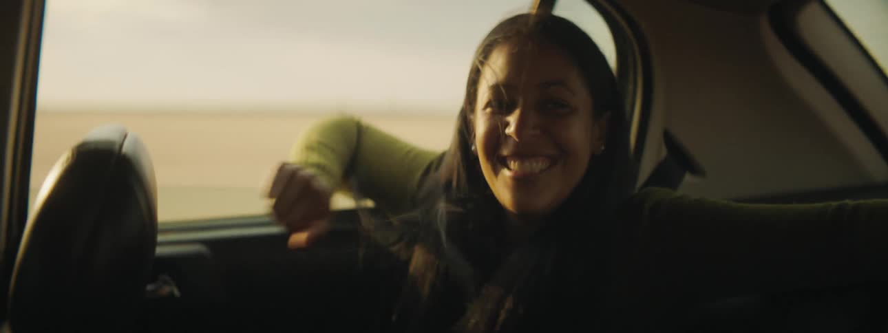 A woman sitting in a car laughs and puts her arm out the window