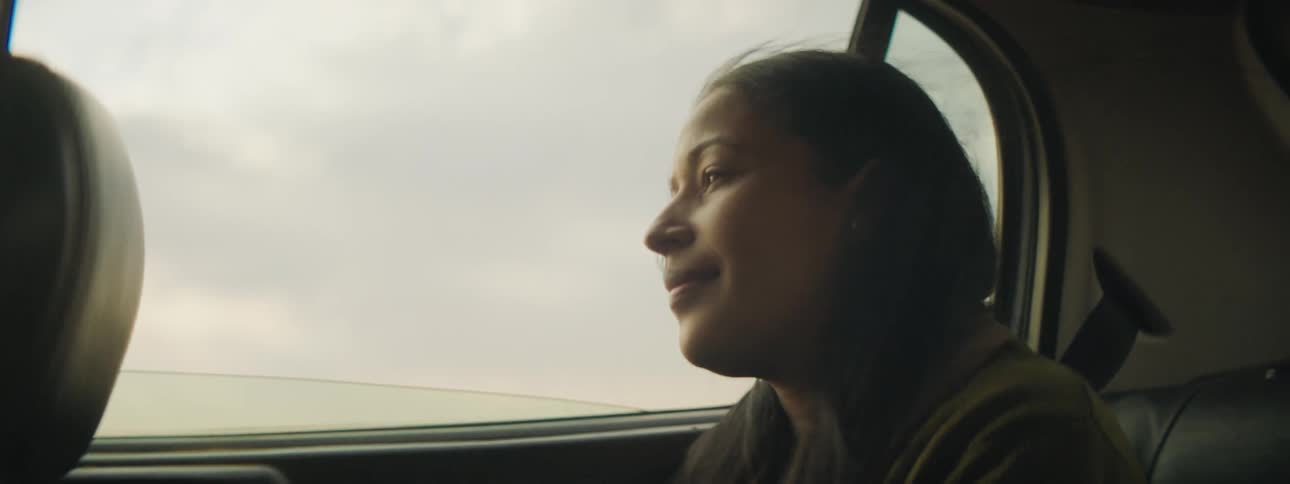 Woman sitting the back of a car smiles slightly